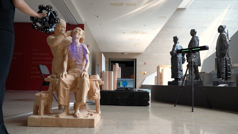 Museum room display with carved mannequins, motion capture camera, and tripod equipment in foreground