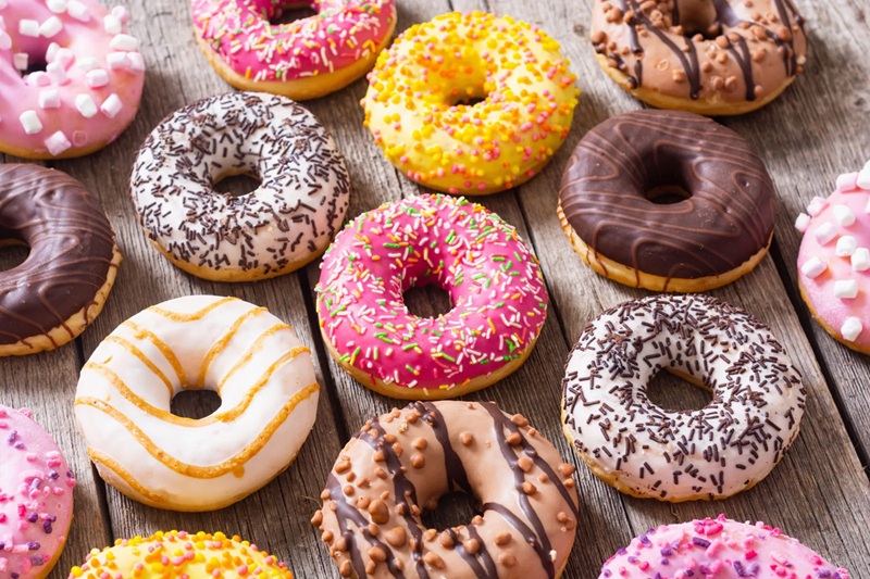 Assorted frosted chocolate and sugar donuts with sprinkles on a rustic wooden table