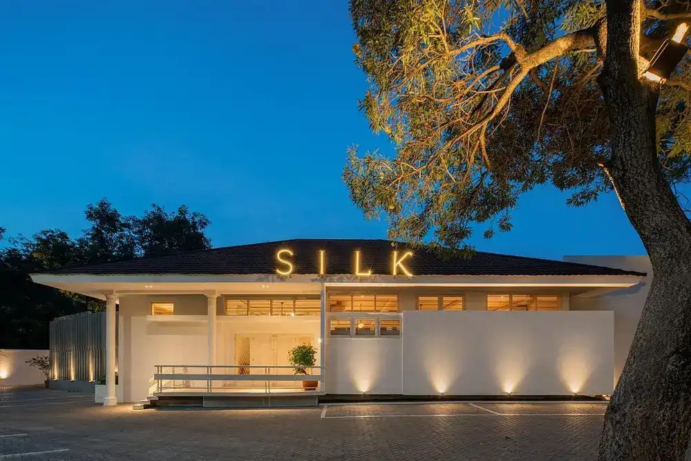 Night view of a modern house with illuminated “SILK” sign, trees, and warm lighting in the entry courtyard