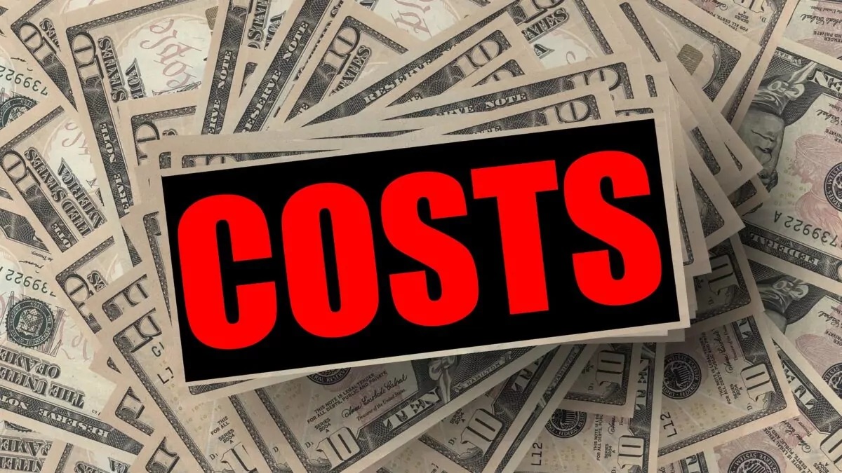 Close-up of “COSTS” text in red and black on a stack of U.S. dollar bills