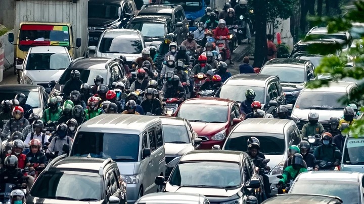 Congested city street filled with motorcycles and cars, dense traffic at rush hour with helmeted riders
