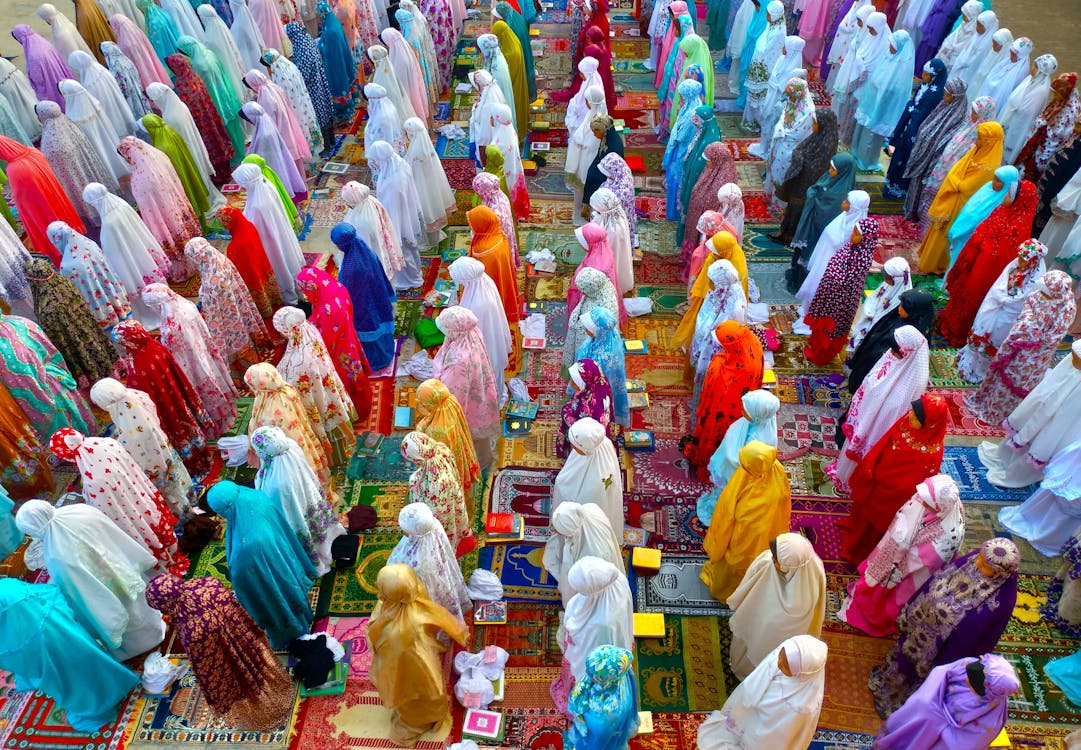 Colorful stalls lined with women in abayas and hijabs standing on patterned rugs in a busy market aisle