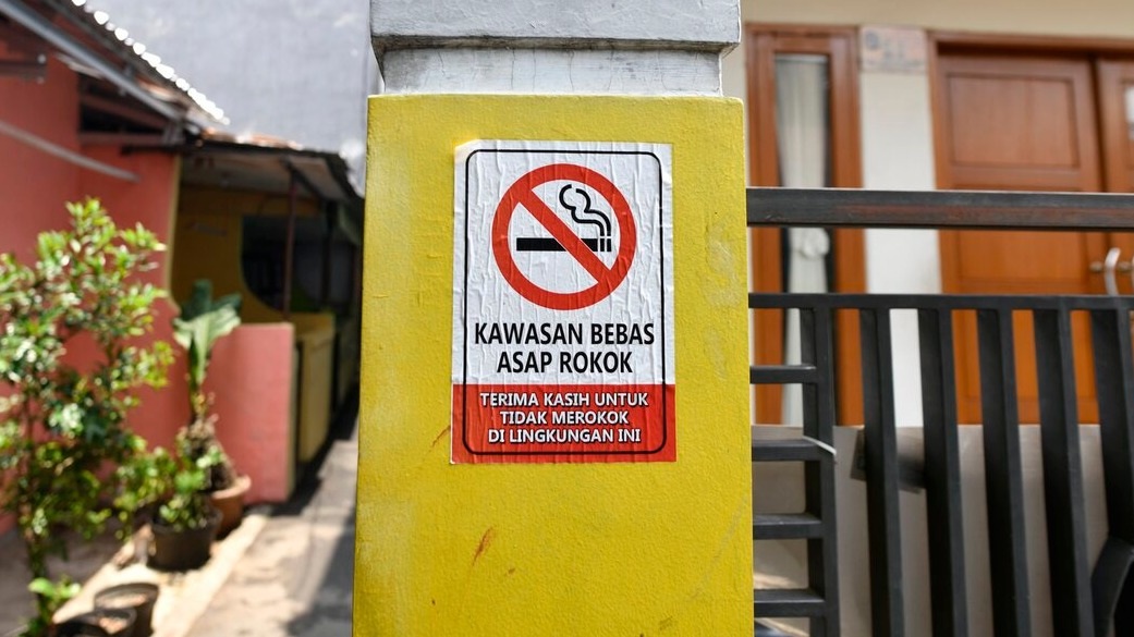 Kawasan bebas asap rokok sign on yellow pillar with no smoking icon and warning text outdoors