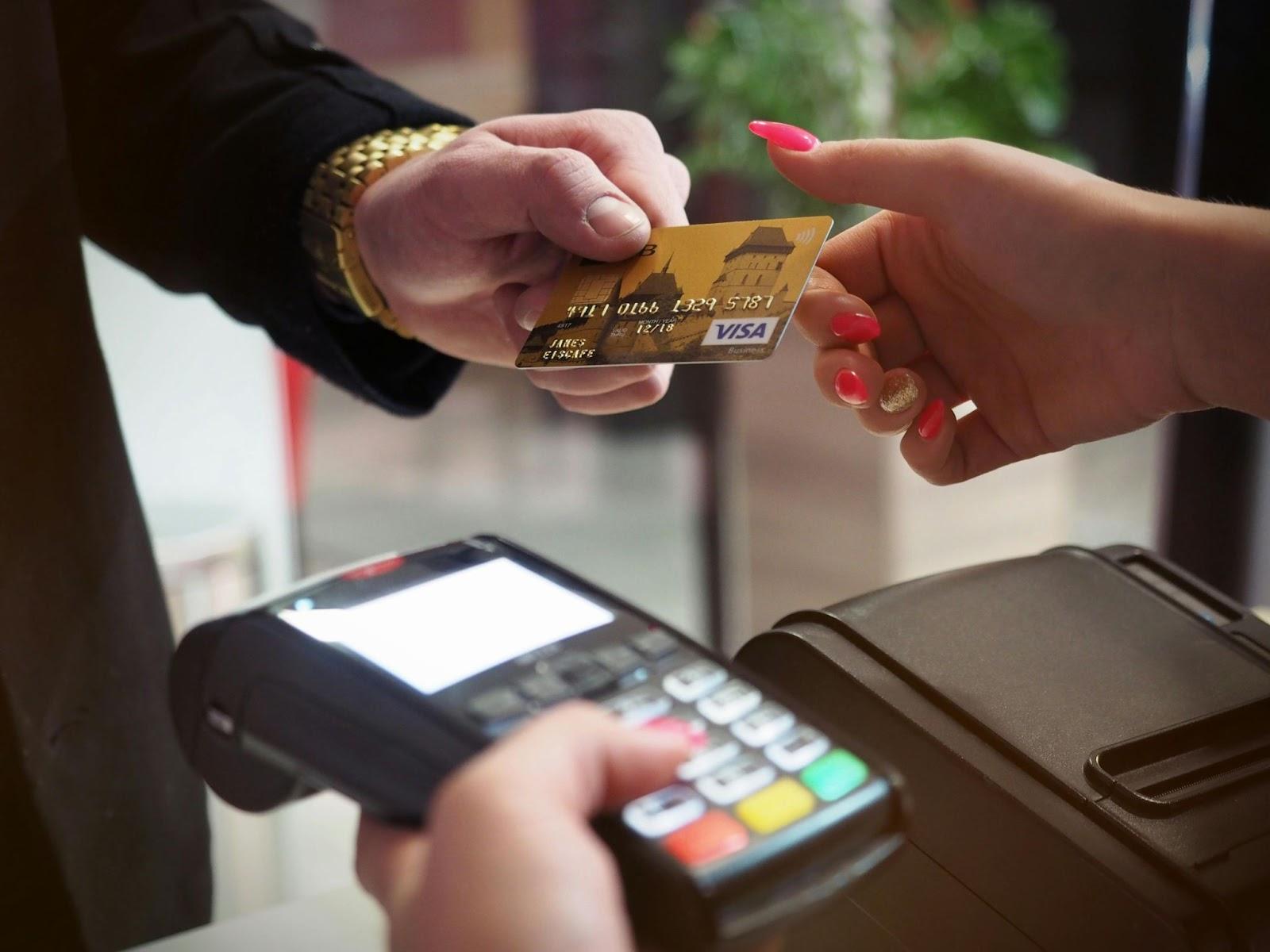 Person handing over a VISA credit card during a card payment at a checkout terminal with keypad visible