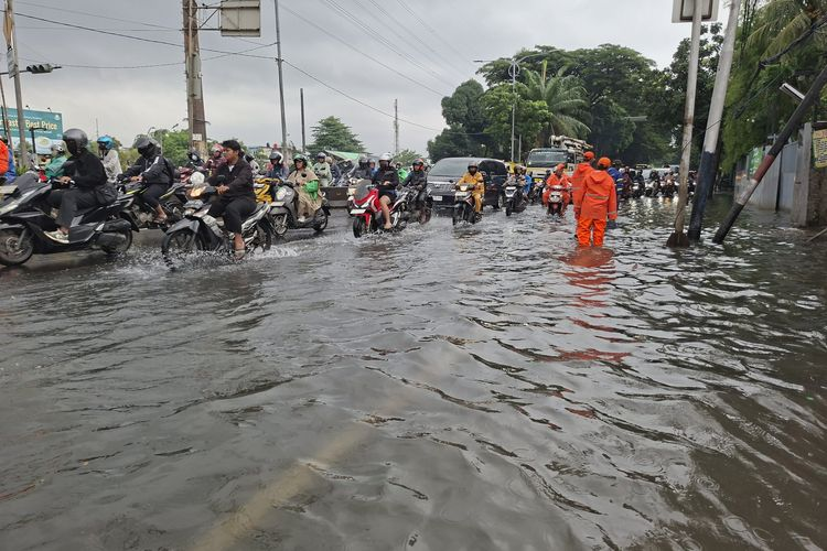 Flooded city street packed with motorcycles and commuters, emergency worker in orange wading through water