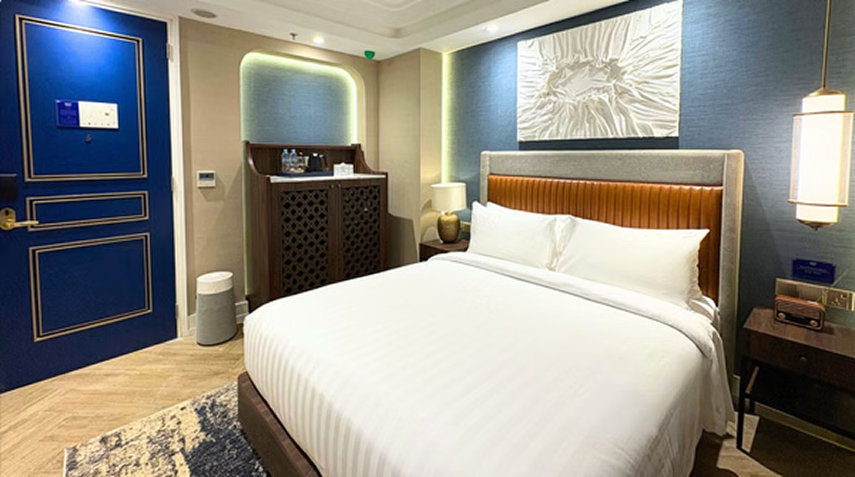 Modern hotel room with blue door, king-size bed, wall art, and warm LED accent lighting