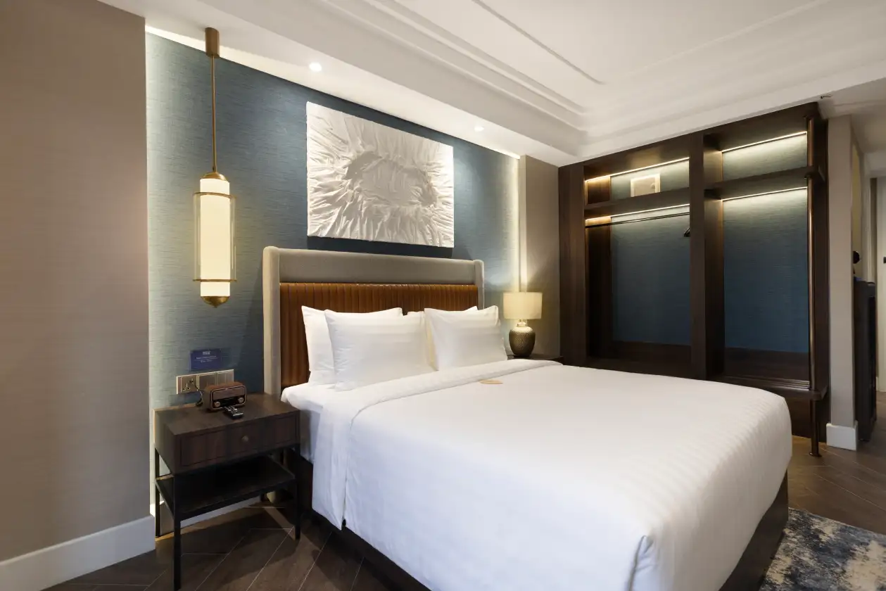 Modern hotel bedroom with neatly made bed, bedside tables, wall art, and warm overhead lighting