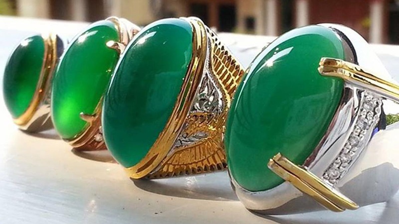 Shiny green gemstone rings with gold and silver settings arranged on a white surface