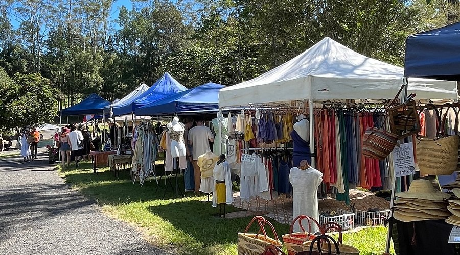 Outdoor market stalls with tents and clothing racks, hats, and woven baskets on a sunny day