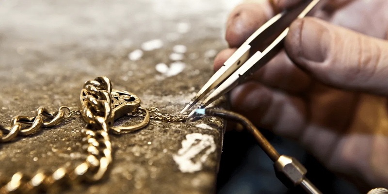 Jewelry repair close-up: gloved hand using tweezers to solder a gold chain on a workbench