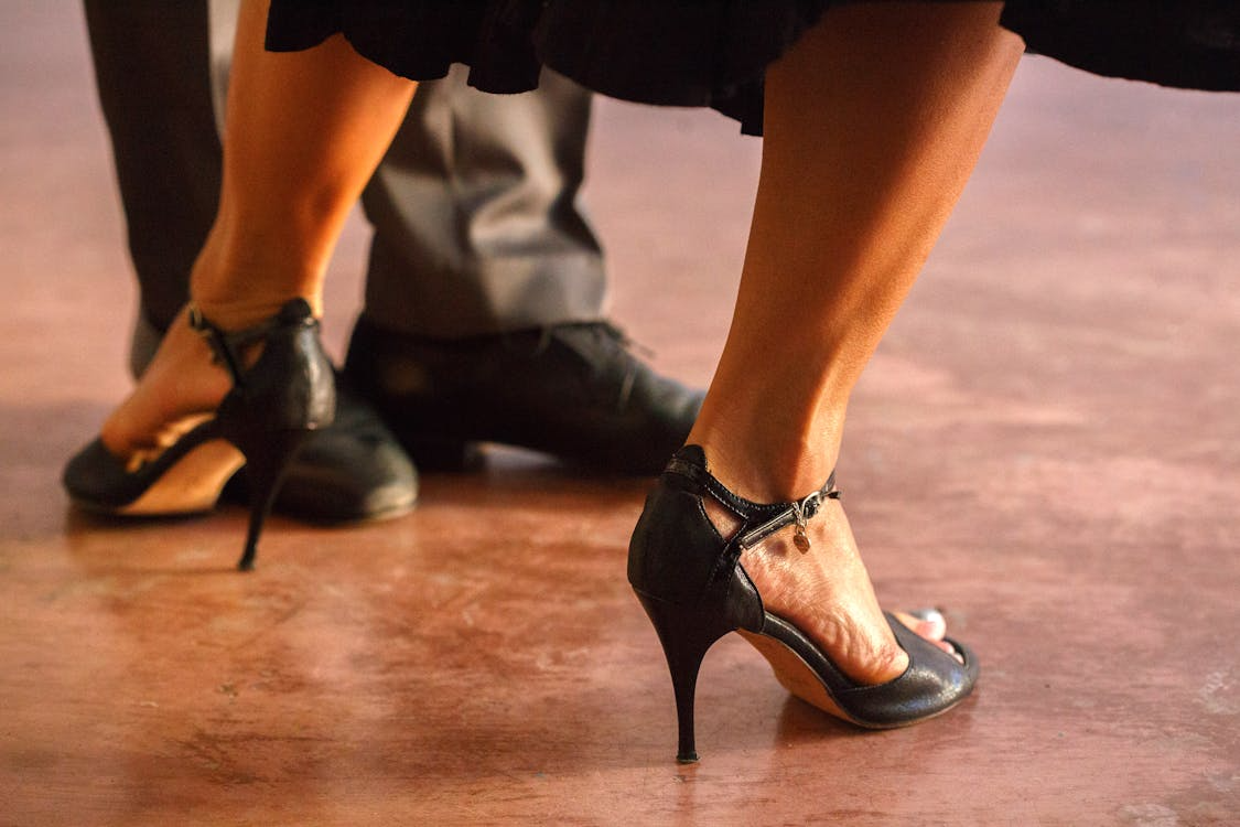 Woman in black high heels walking indoors on wooden floor, close-up of feet and legs