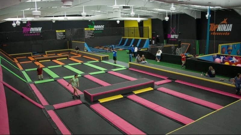 Indoor trampoline park with multiple spring lanes, foam blocks, and participants jumping on colorful mats