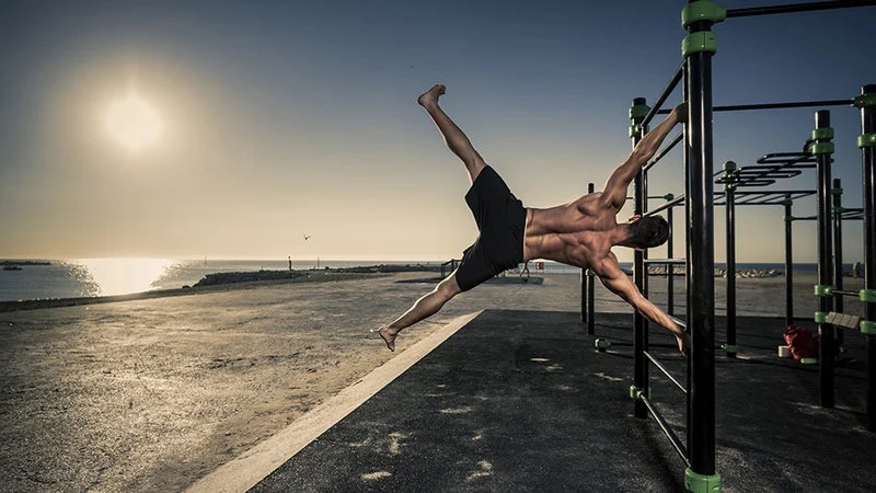 Two athletes performing a handstand stretch on outdoor calisthenics bars at sunset by the beach