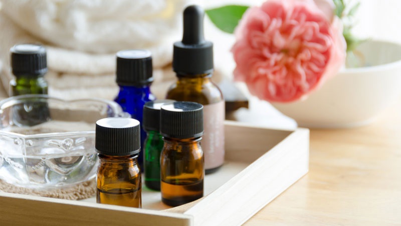Essential oil bottles in glass droppers on a wooden tray with flowers and soft background blur