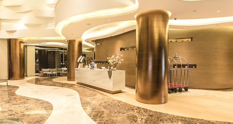 Modern hotel lobby interior with marble floors, gold columns, and a reception desk with luggage carts