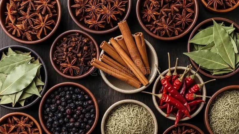Bowls of spices and herbs: bay leaves, star anise, cinnamon sticks, chili peppers, peppercorns, and dried herbs on wood