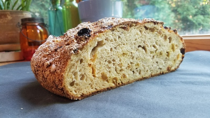 Rustic sliced sourdough bread with open crumb texture on a blue tablecloth, background jars and greenery