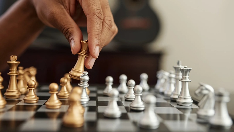 Chessboard with a hand placing a chess piece among gold and silver pieces during a strategy game