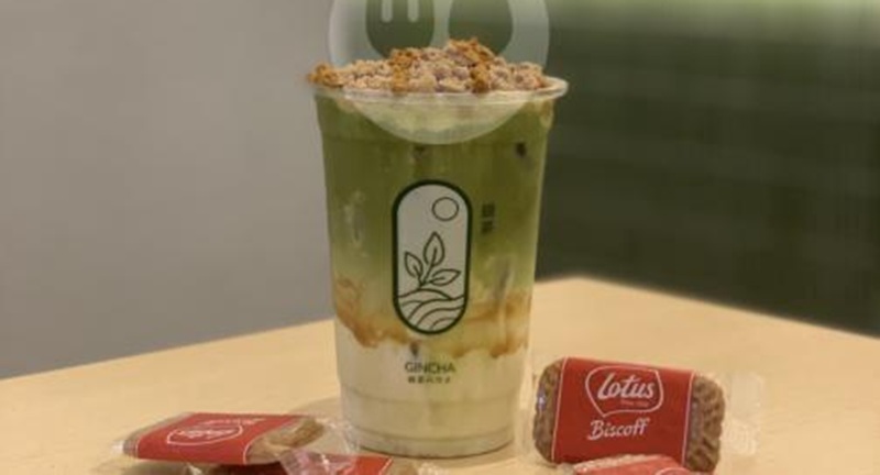 Green tea drink in a reusable cup with granola topping, beside Lotus Biscoff biscuits on a table