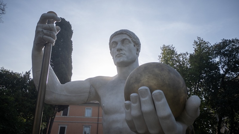 Bronze statue holding a microphone and raised fist outdoors under a blue sky