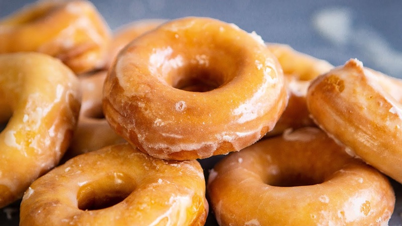 Freshly fried donuts with sugar glaze piled close-up on a tray, showing several doughnut holes
