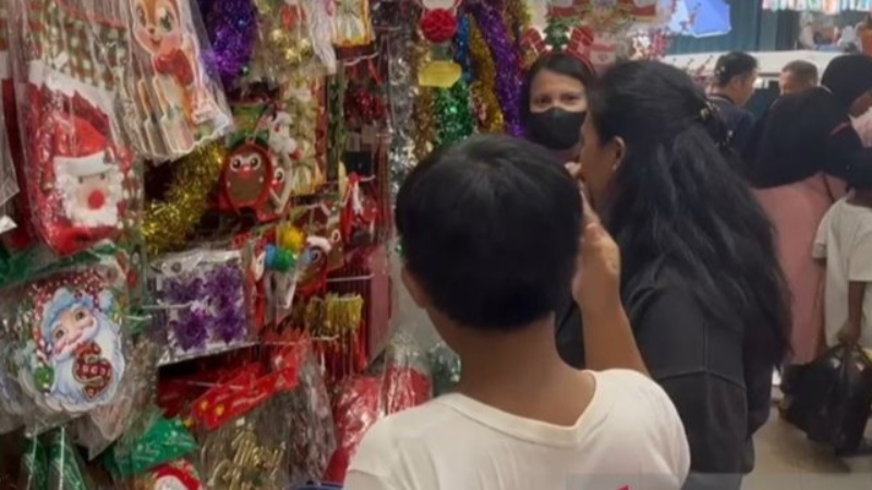Crowded holiday market with shoppers looking at colorful Christmas decorations and lights in the aisle