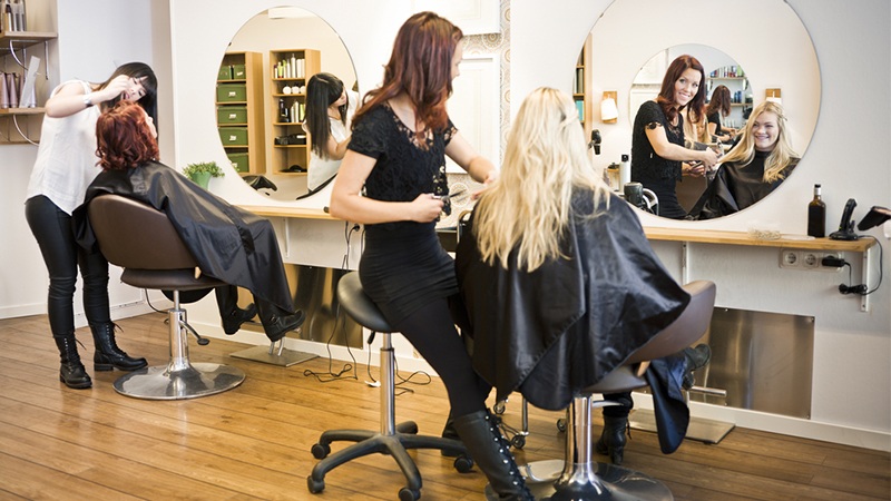 Hairdresser cutting and styling a client’s hair in a salon with round mirrors and styling chairs