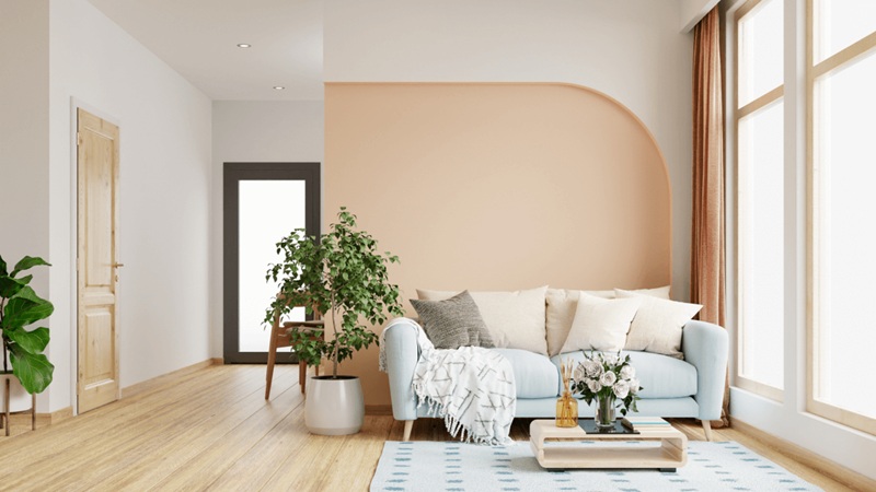Bright modern living room with light wood floor, blue sofa, plants, and large arched wall.