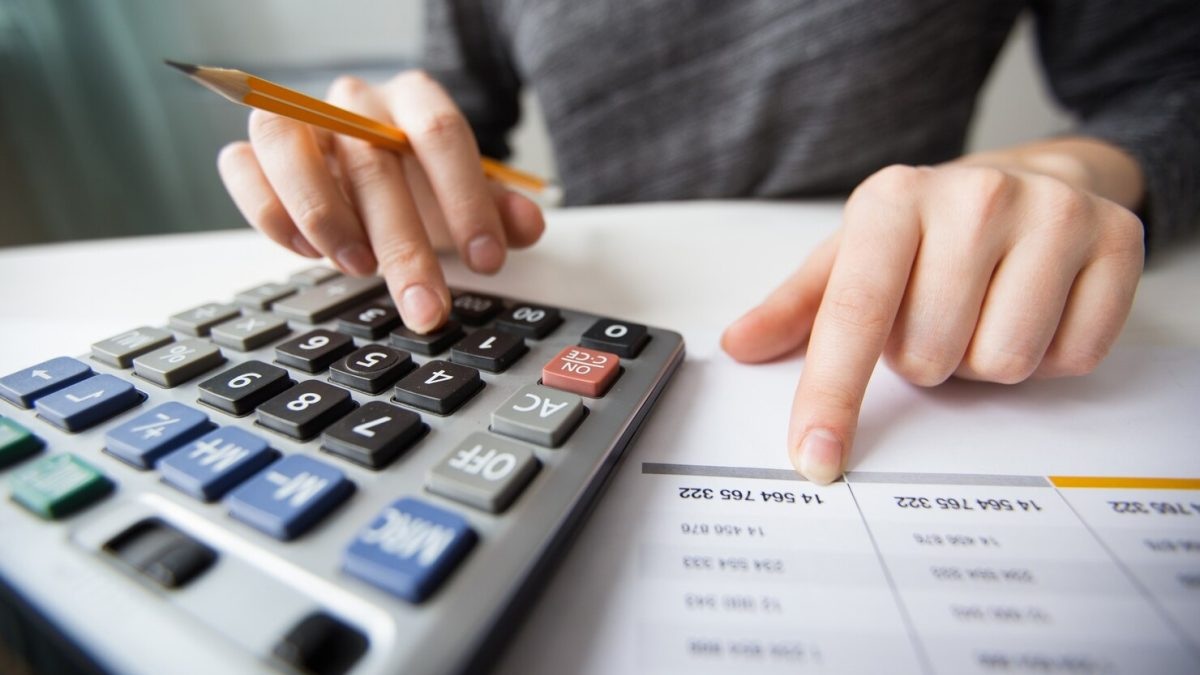 Hands using a calculator and pencil with printed financial statements on a desk, calculating totals and numbers