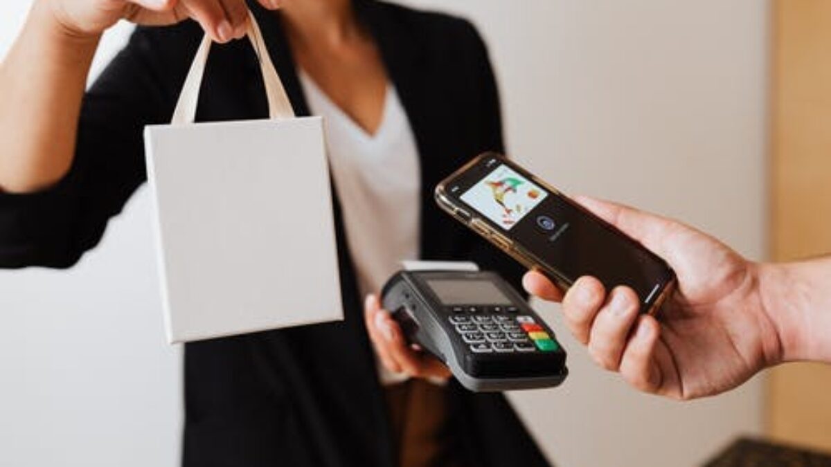 Retail worker handing a smartphone with contactless payment terminal and a shopping bag in hand