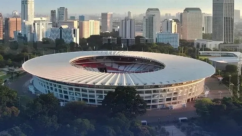 Aerial view of a large stadium with a circular roof and skyline of high-rise buildings in the background