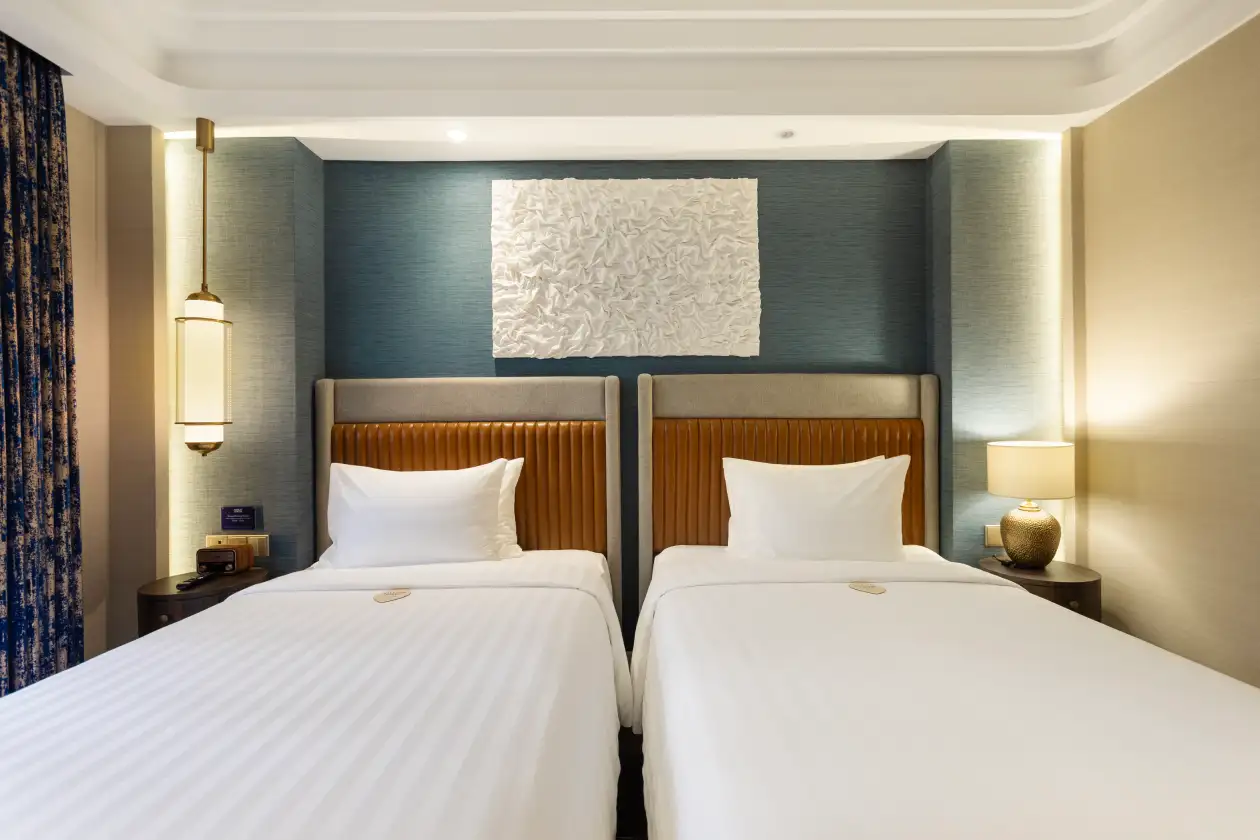 Modern hotel room with two beds, white linens, bedside lamps, and blue accent wall backdrop