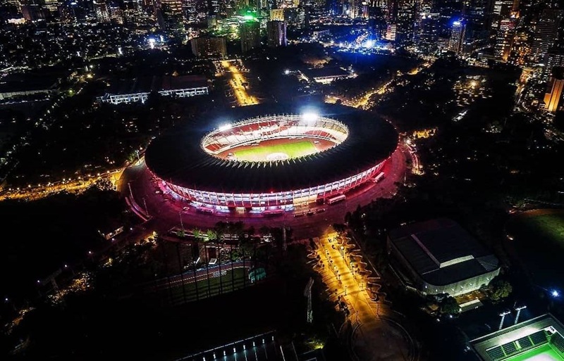 Aerial view of a brightly lit stadium at night with surrounding city lights and roads.