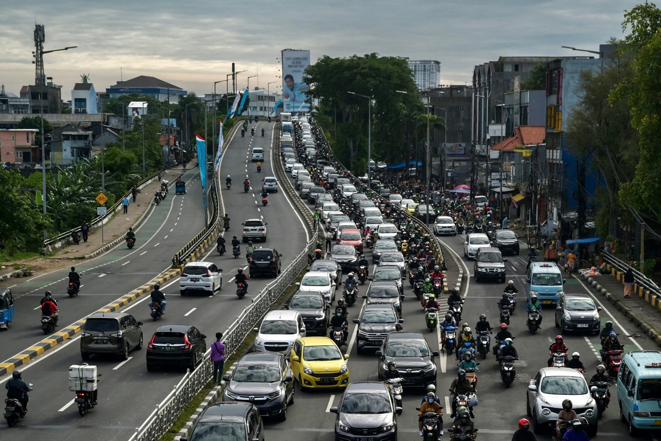 Busy multi-lane highway with heavy traffic of cars and motorcycles under cloudy sky in a city