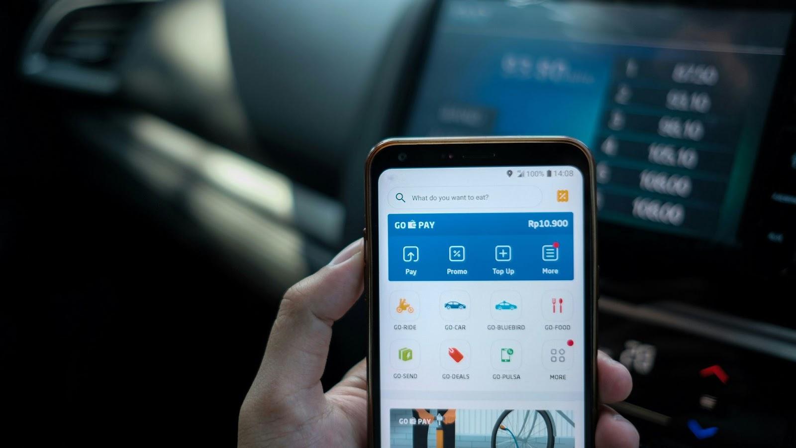 Hand holding a smartphone showing GoPay menu with payment, promo, and top up options