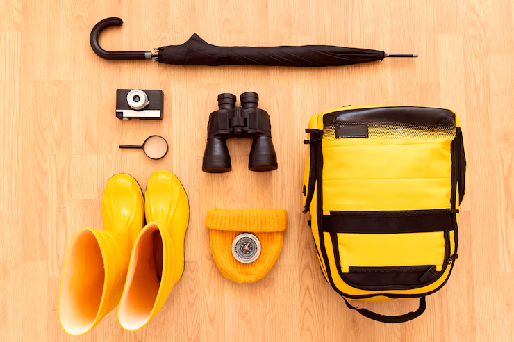Yellow rain gear flat lay: umbrella, binoculars, binoculars strap bag, rubber boots, flashlight, binoculars, gloves