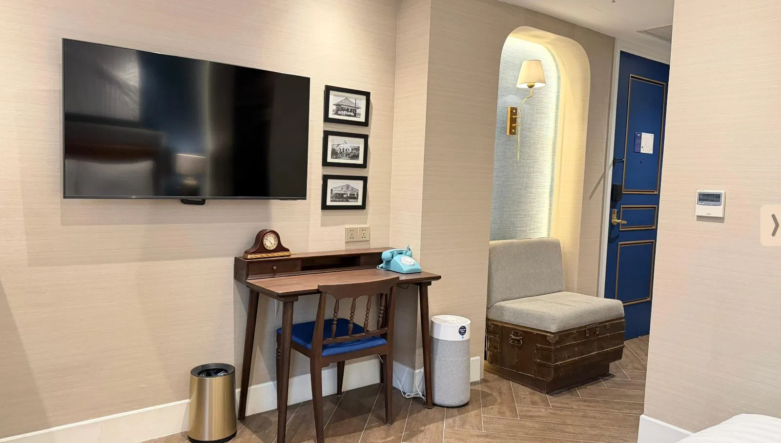Modern hotel entry area with arched doorway, gray chair, wall TV, console table, and reading lamp in warm lighting