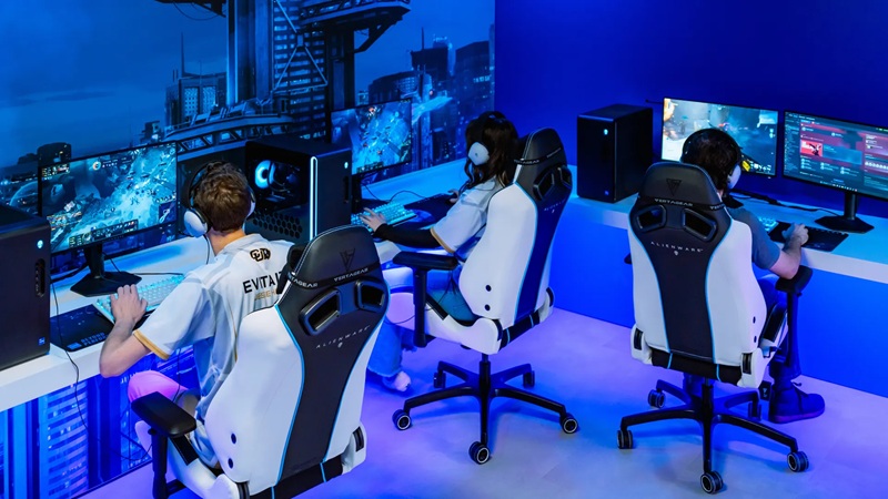 Esports gaming lab with players in white VR headsets at PCs, multiple monitors, blue-lit control room scene