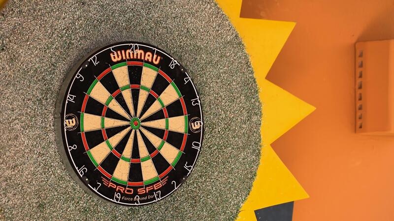 Darts board with bullseye and numbered ring target on artificial turf, with colorful wall and star backdrop nearby