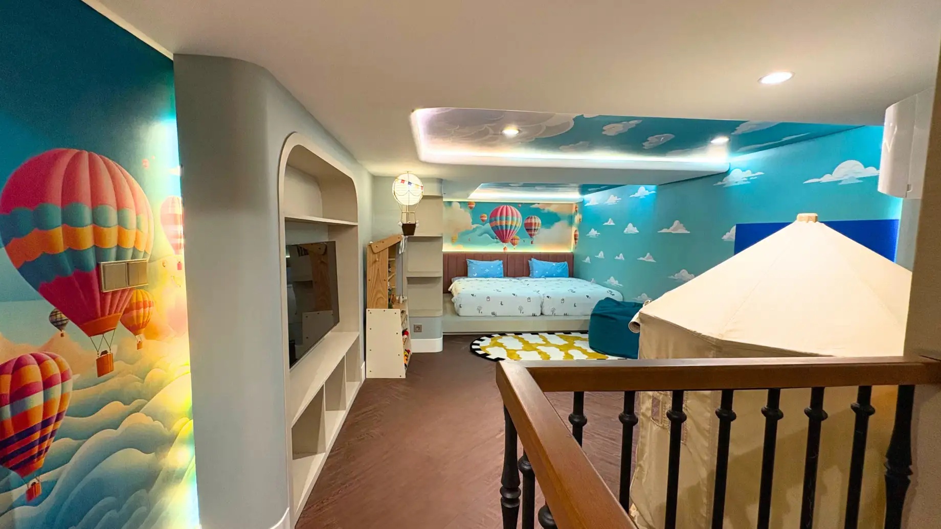 Children’s play bedroom with blue wall mural of hot air balloons, canopy bed, shelves, and night lights