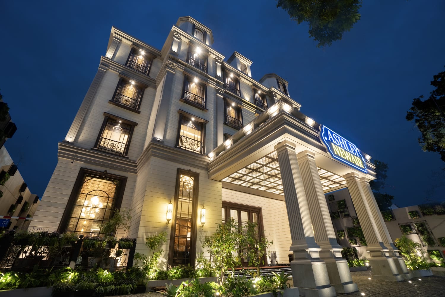 Astoria Mews building exterior at dusk with illuminated windows, columns, and entrance sign