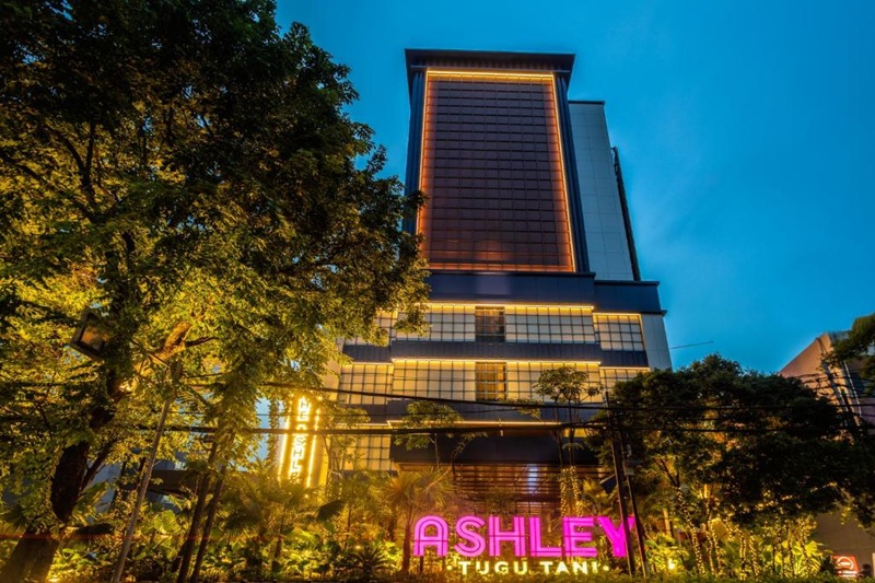 Ashley Tugu Tani building facade at dusk with neon sign and trees along the street, Indonesia