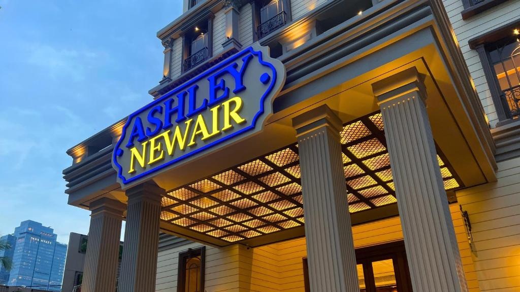 Ashley Newair storefront sign above columns at dusk with warm indoor lighting and balcony railings