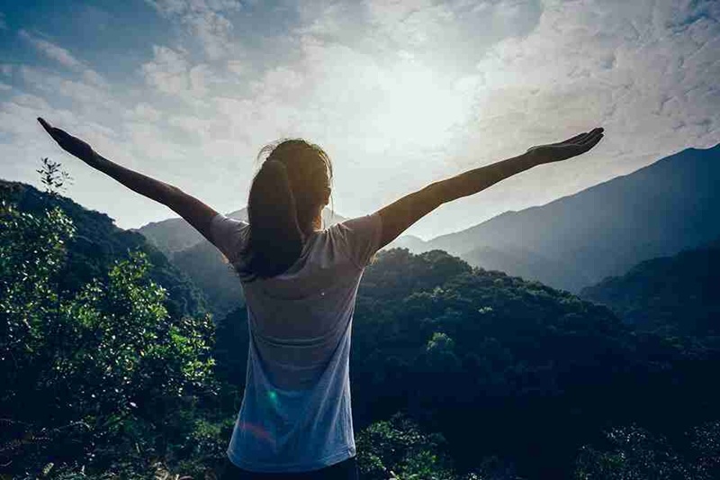 Woman with arms outstretched in scenic mountain valley at sunrise, hiking outdoors in nature