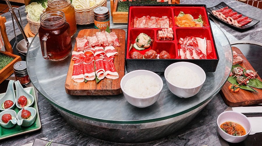 Assorted raw meats on ice trays for a BBQ buffet, with bowls of sauces and sliced peppers and herbs