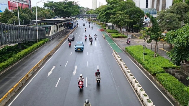 Multi-lane city road with motorbikes and cars traveling through lush greenery and tall buildings