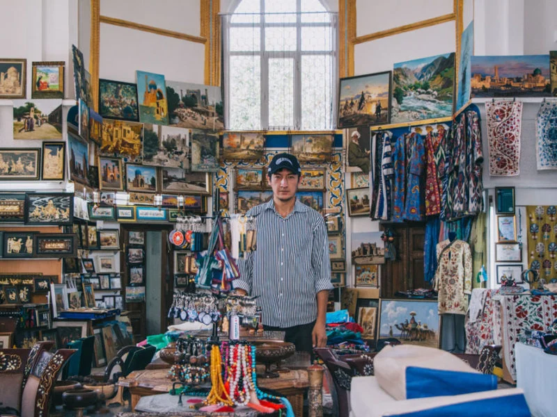 shop owner standing in a colorful souvenir store aisle, framed photos and textiles covering walls