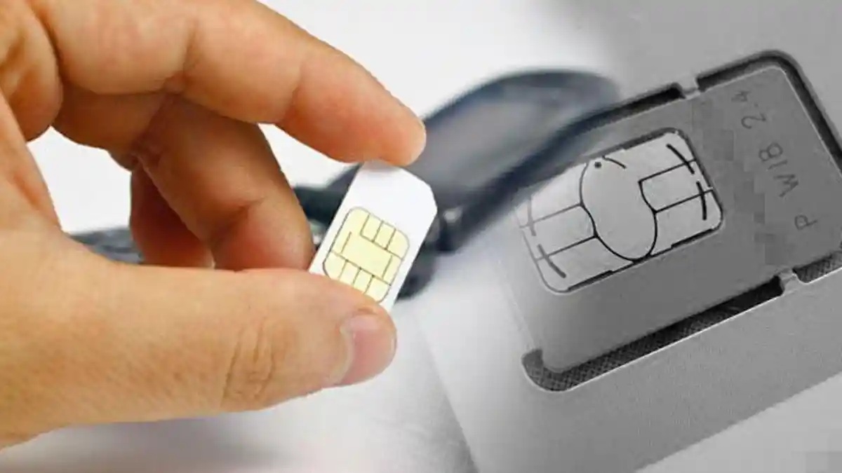 Hand inserting a SIM card into a card reader device with a chip visible and smartphone in background