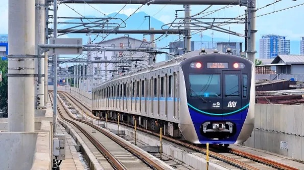 Oncoming modern metro train on tracks at an electrified urban railway station, city skyline in background