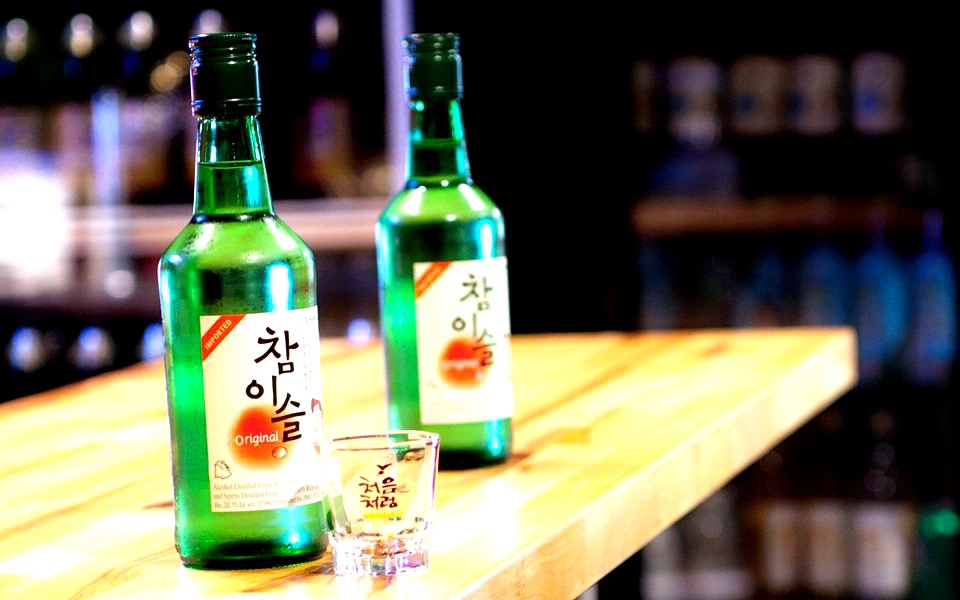 Two bottles of Korean soju with a small shot glass on a bar counter in a dimly lit background